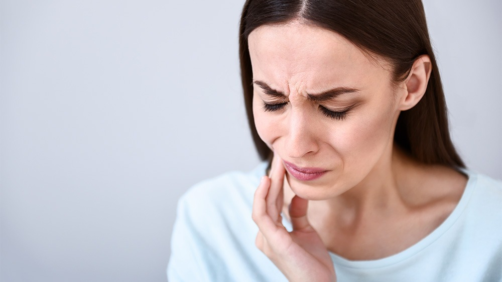 Junge Frau greift sich an die Wange, weil sie offensichtlich Zahnschmerzen hat.